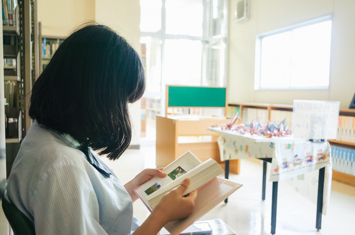 図書室で本を開く制服姿の彼女。