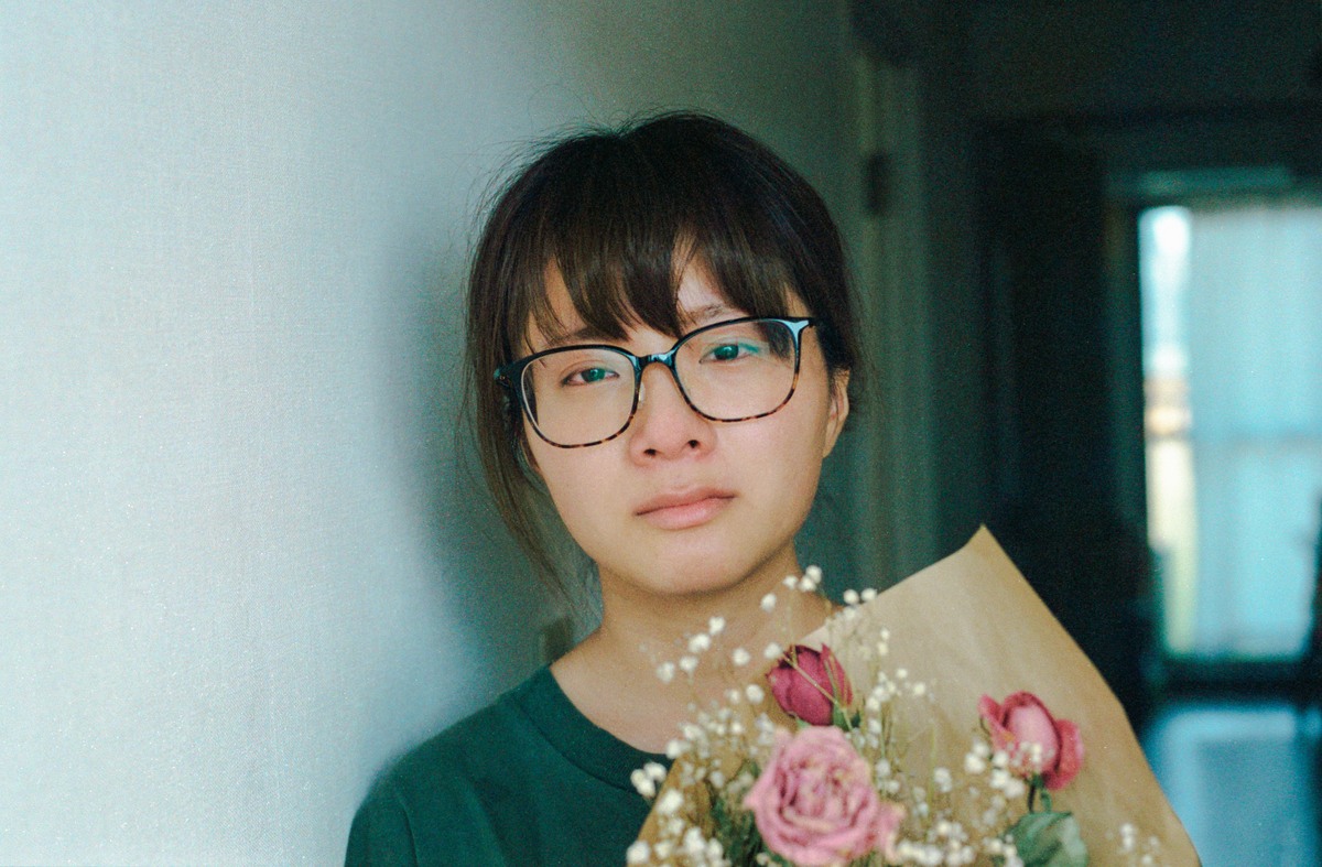 花束を抱え、眼鏡をかけてこちらを見つめる彼女。